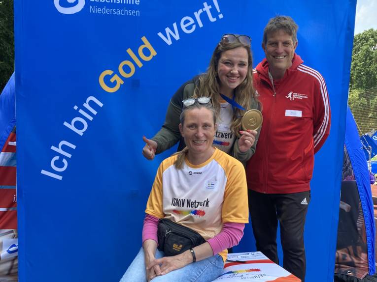 Drei Personen vor einem Plakat mit der Aufschrift "Ich bin Gold wert"